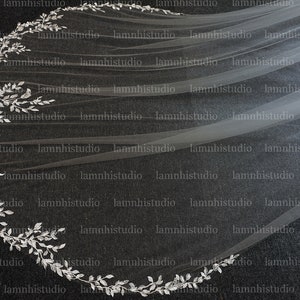 May include: A long, flowing white bridal veil with a silver leaf trim. The veil is sheer and lightweight, with a decorative border of silver leaves. The design is elegant and suitable for a wedding.