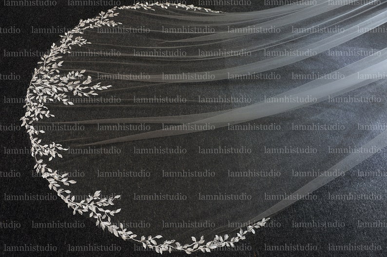 May include: A long, flowing white bridal veil with a silver leaf trim. The veil is sheer and lightweight, with a decorative border of silver leaves. The design is elegant and suitable for a wedding.