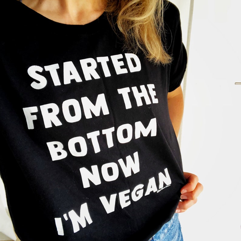 May include: Black t-shirt with white text that reads "Started from the bottom now I'm vegan".