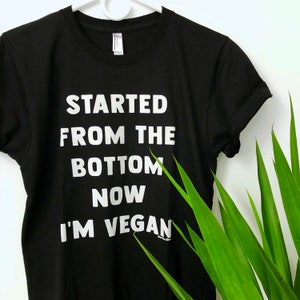 May include: Black t-shirt with white text that reads "Started from the bottom now I'm vegan".