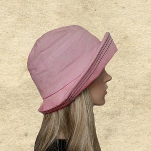 May include: A pink sun hat with a black trim. The hat has a wide brim and is made of a soft, lightweight fabric.