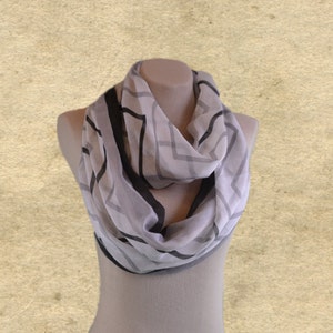 May include: A gray and black patterned infinity scarf made of sheer fabric. The scarf is draped around a mannequin's neck.