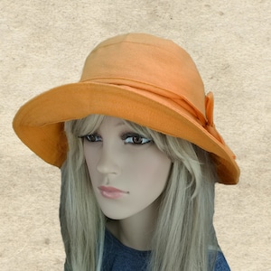 May include: A wide-brimmed sun hat in a bright orange color. The hat has a simple design with a small bow on the side.