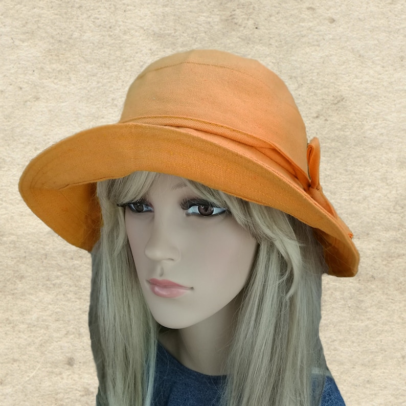 May include: A wide-brimmed sun hat in a bright orange color. The hat has a simple design with a small bow on the side.