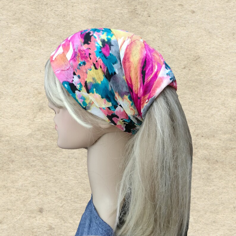 May include: A colorful floral headband with pink, yellow, blue, and white flowers on a white background. The headband is worn by a person with blonde hair.