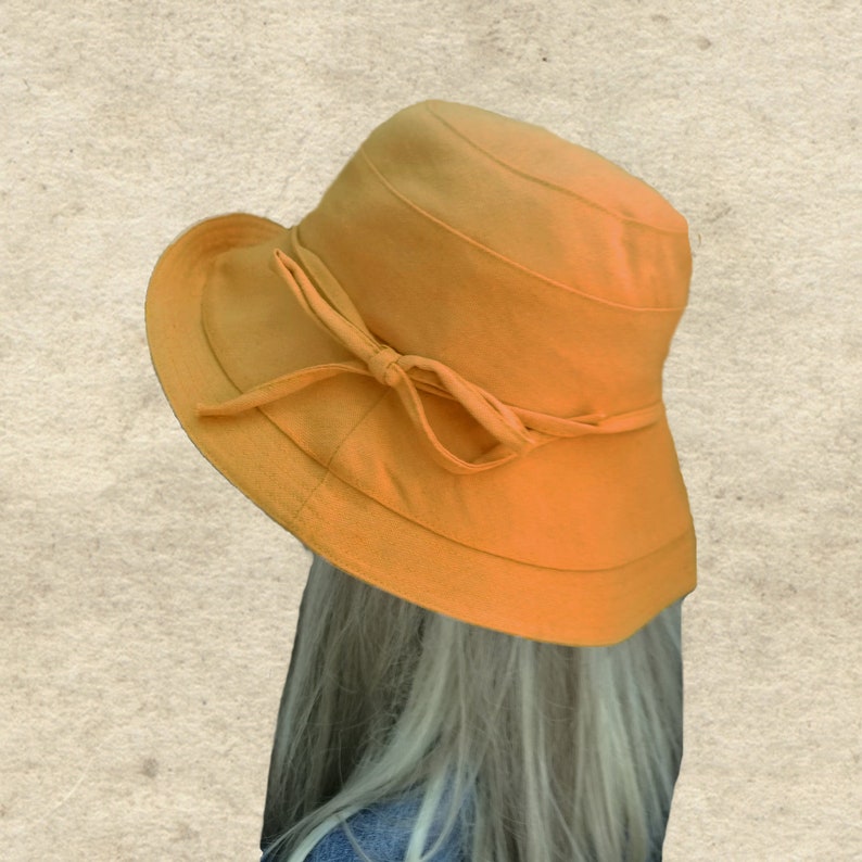 May include: A wide-brimmed sun hat in a solid mustard yellow color. The hat has a simple design with a bow tied at the front.