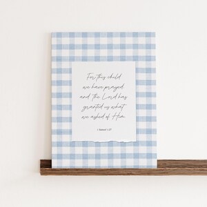 Op de afbeelding: Een rechthoekige wandkunstprint met een lichtblauwe en witte gingham-achtergrond. In het midden bevindt zich een wit papieren inzetstuk met gescheurde onderranden, waarop de zwarte cursieve tekst staat: For this child we have prayed, and the Lord has granted us what we asked of Him. 1 Samuel 1:27.