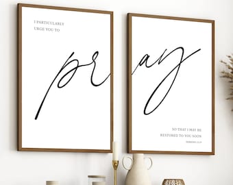 May include: Two framed art prints with the word "pray" in elegant black script on a white background. One print reads "I particularly urge you to pray." The other reads "So that I may be restored to you soon."