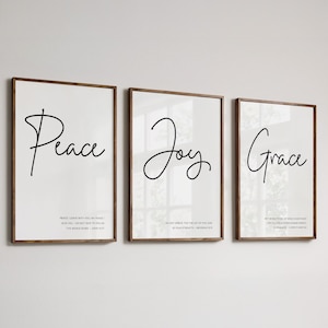 May include: Three framed prints with white backgrounds and black calligraphy. The prints feature the words "Peace", "Joy", and "Grace" with corresponding Bible verses below each word.