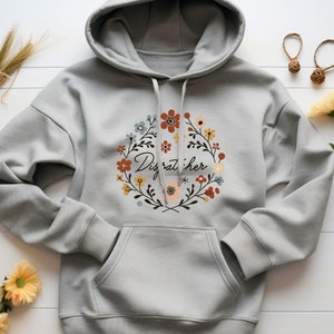 May include: Gray hooded sweatshirt with a floral wreath design and the text "Disrupt her" in the center.