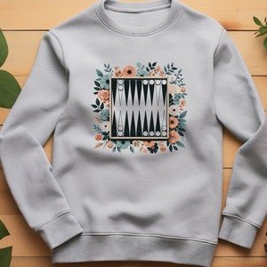 May include: A light gray sweatshirt with a floral design featuring a black and white backgammon board in the center.