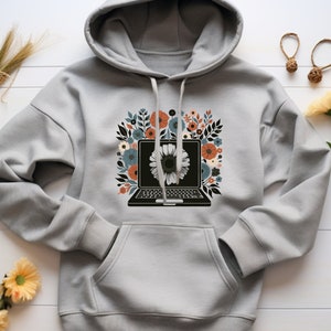 Puede incluir: Una sudadera con capucha gris con un diseño floral que presenta un portátil con una flor en la pantalla. Las flores son en tonos naranja, rojo, azul y blanco.