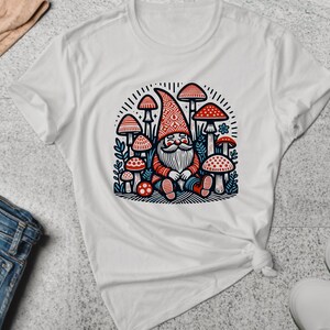 May include: White t-shirt with a colorful illustration of a gnome sitting among mushrooms. The gnome is wearing a red and white hat and has a white beard. The mushrooms are red and white with blue and green accents.