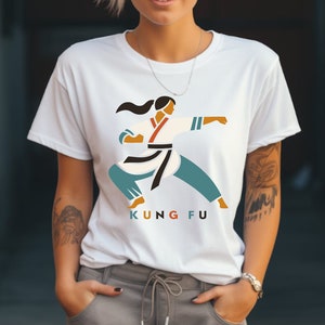 Peut inclure: T-shirt blanc avec un motif représentant une femme en position de karaté. Le motif est dans des tons d'orange, bleu, noir et blanc. Le texte "KUNG FU" est imprimé sous le motif.