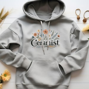May include: Gray hooded sweatshirt with a floral design and the word "Ceramist" printed on the front.