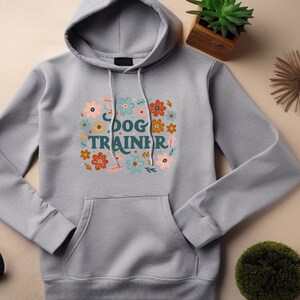 May include: Grey hooded sweatshirt with a floral design and the text "DOG TRAINER" in a colourful font.