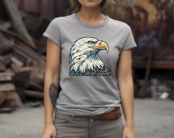 May include: A gray t-shirt with a vintage-style illustration of a bald eagle's head. The eagle's head is facing right and has a yellow beak and yellow and blue feathers.
