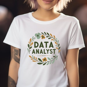 May include: White t-shirt with a green and gold floral wreath design and the text "DATA ANALYST" in the center.