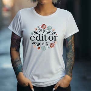 May include: White t-shirt with a floral design and the word "editor" in black text.