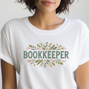 May include: White t-shirt with a green floral design and the word "BOOKKEEPER" in green text.