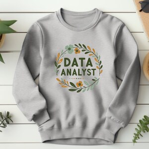 May include: A gray sweatshirt with a floral wreath design and the text "DATA ANALYST" in the center.
