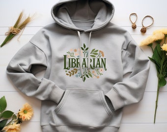 Puede incluir: Una sudadera con capucha gris con un diseño floral y la palabra "LIBRARIAN" en letras verdes.
