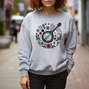 May include: A gray sweatshirt with a floral design featuring a banjo. The banjo is black with a white rim and strings. The flowers are in shades of blue, red, and yellow.