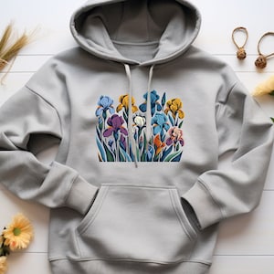 Puede incluir: Una sudadera con capucha gris con un estampado floral colorido de iris. El estampado presenta una variedad de colores, incluyendo azul, morado, amarillo y blanco.
