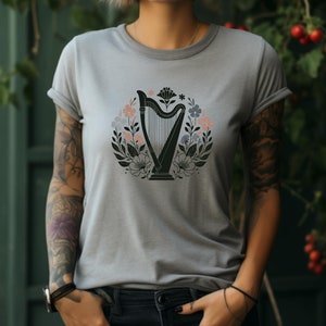 May include: A gray t-shirt with a black and white illustration of a harp surrounded by flowers. The flowers are in shades of pink, blue, and green.