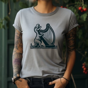 May include: A gray t-shirt with a black and white illustration of a dinosaur playing a harp.