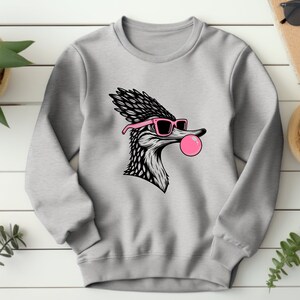 May include: A grey sweatshirt featuring a black and white illustration of a bird wearing pink sunglasses and blowing a pink bubble.