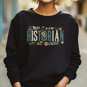 May include: Black sweatshirt with a floral design and the word "HISTORIAN" in teal and cream lettering.