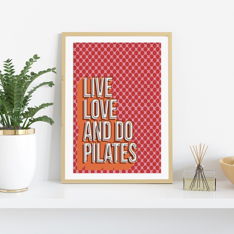 May include: A framed print with a red and pink polka dot background and the text "LIVE LOVE AND DO PILATES" in white letters with a black outline.