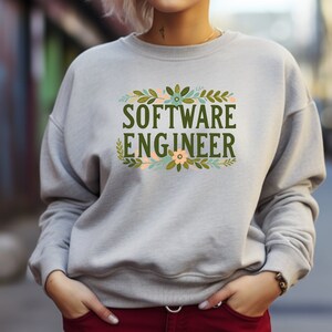 Puede incluir: Una sudadera gris con un diseño floral y el texto "SOFTWARE ENGINEER" en letras verdes.