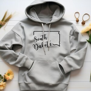 May include: Gray hooded sweatshirt with a black outline of the state of South Dakota and the text "South Dakota" in black cursive lettering.
