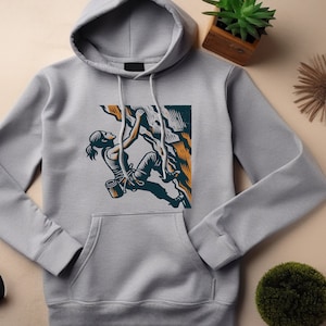 Può includere: Una felpa con cappuccio grigia con una stampa grafica di una persona che fa arrampicata. La grafica è in stile vintage con colori arancio, giallo e blu.