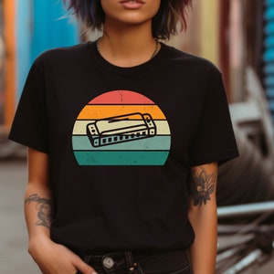 May include: A black t-shirt with a vintage-style graphic of a harmonica in front of a sunset. The graphic has a distressed look with faded colors.