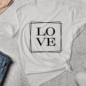 May include: White t-shirt with a black graphic of the word "LOVE" in a double square frame.