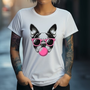 May include: White t-shirt featuring a graphic of a Boston Terrier wearing pink sunglasses and blowing a pink bubble. The dog's face is black and white. The t-shirt has short sleeves and a crew neck.