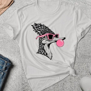 May include: White t-shirt with a black and white illustration of a bird wearing pink sunglasses and blowing a pink bubble.