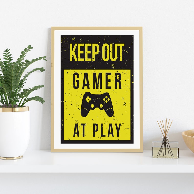 May include: A yellow and black sign with the text "Keep Out Gamer At Play" and a black video game controller graphic.