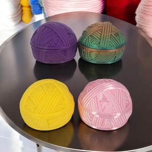 May include: Four colorful yarn ball shaped boxes. The boxes are purple, green, yellow, and pink. The boxes are made of a smooth, shiny material and have a textured yarn design.