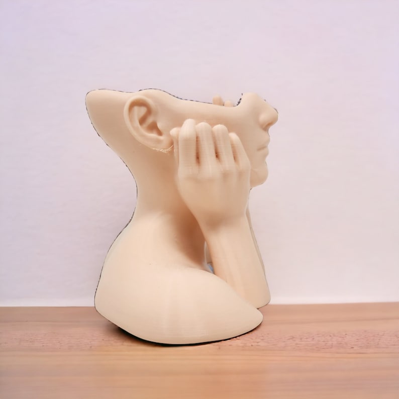 Op de afbeelding: Een beige keramische sculptuur van een hoofd en schouders van een persoon met de handen op de kin. De sculptuur is ontworpen om een plantenbak te zijn, met een opening in de bovenkant van het hoofd.