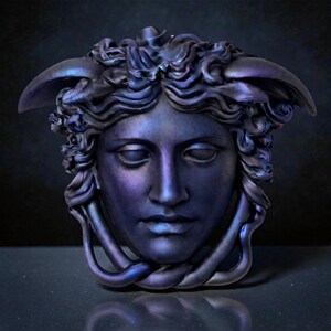 A dark purple and blue iridescent Medusa head sculpture with serpent hair and a braided chin piece, set against a dark background.