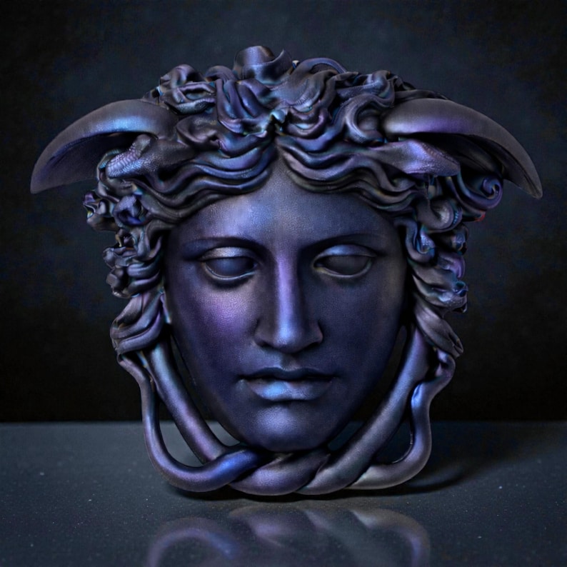 A dark purple and blue iridescent Medusa head sculpture with serpent hair and a braided chin piece, set against a dark background.