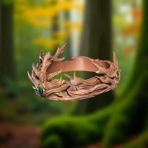 A brown, textured crown with a green gem is suspended in mid-air against a blurred green and yellow forest background.