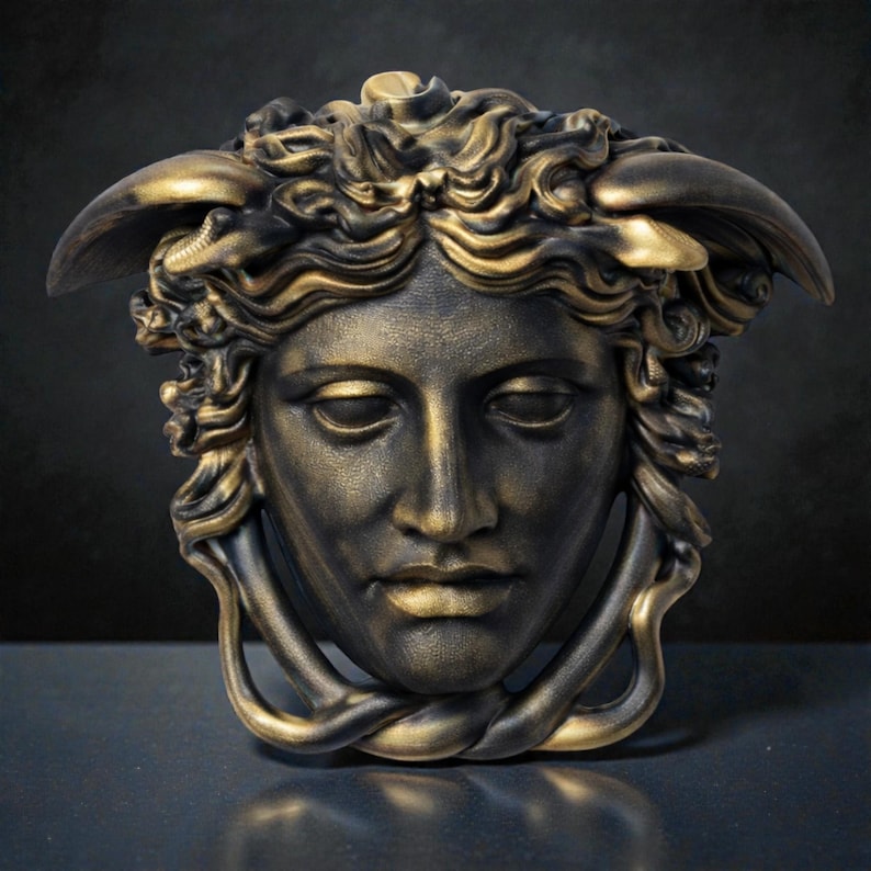 A bronze Medusa head sculpture with snakes for hair and under the chin, against a dark background.