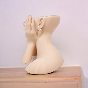 Op de afbeelding: Een wit keramisch beeld van een mensenhoofd en schouders, met een hand die het gezicht bedekt. Het beeld staat in een contemplatieve houding.