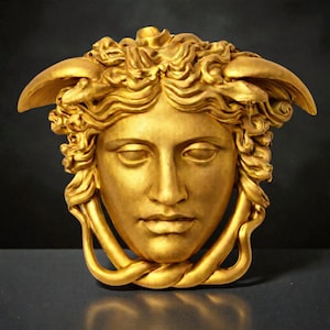 A gold Medusa head sculpture with snakes for hair and under the chin, against a dark background.