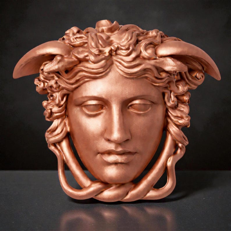 A copper-colored Medusa head sculpture with serpent hair and a braided chin piece, set against a dark background.